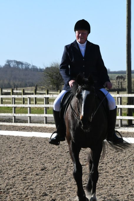 A rider in formal attire on a horse in a riding arena with a countryside background.