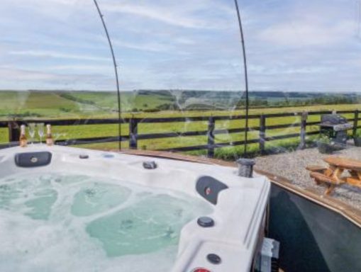 Hot tub on a deck overlooking green fields and a clear sky.