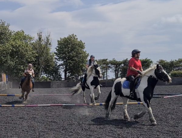 Two riders on horses navigate an outdoor riding arena under a blue sky.