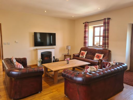 Cosy living room with leather sofas, a coffee table, and a wall-mounted TV.