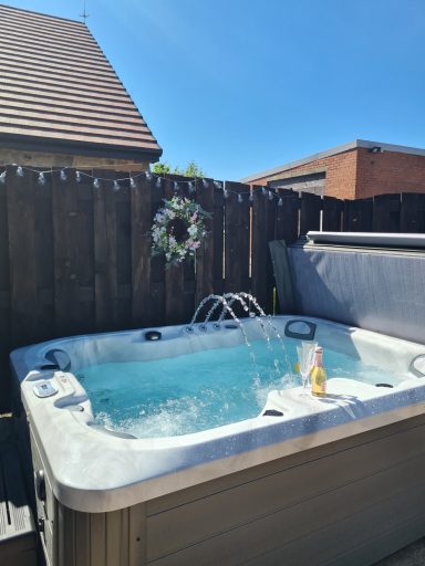 Hot tub with bubbling water in a sunny garden setting, surrounded by wooden fencing.